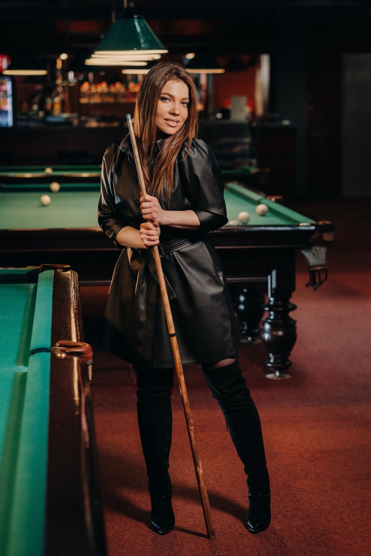 A girl with a cue in her hands is standing in a billiard club.Russian billiards